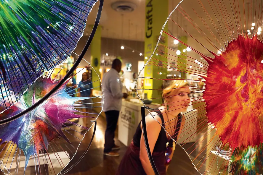 a woman in a black dress peers at a beautiful piece of orange and clear glass art at Florida CraftArt gallery in St. Pete