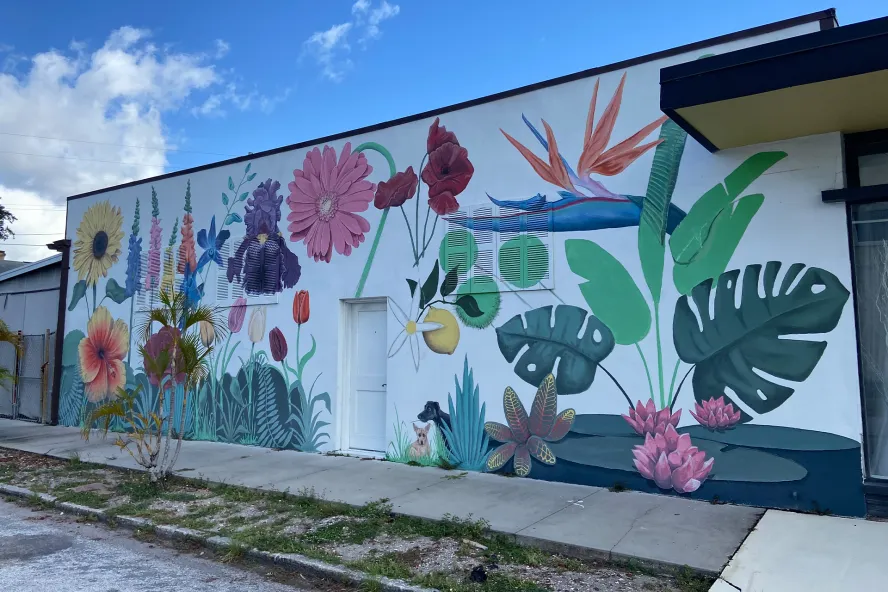Large flower street mural with white background featuring Florida-inspired green palms, colorful spring flowers, tulips and two dogs. 