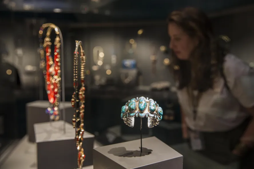 a woman looks at a glass case of Native American jewelry including a turquoise bracelet at the James Museum