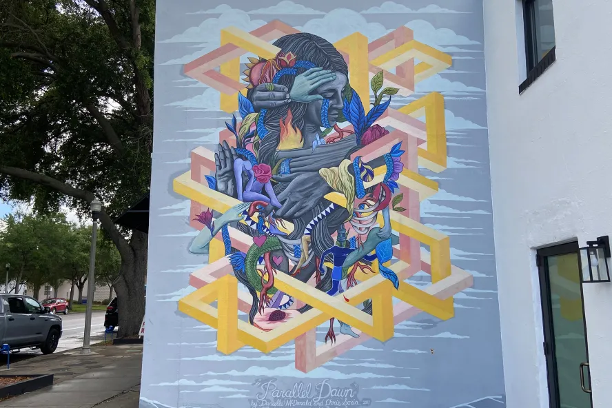 Wall mural by Danielle McDonald and Chris Soria in the MLK North district in St. Pete featuring a woman being held but multiple hands.
