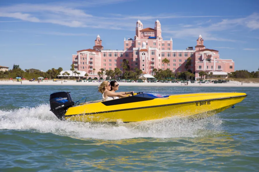 Two people in a yellow speedboat in front of the Don CeSar