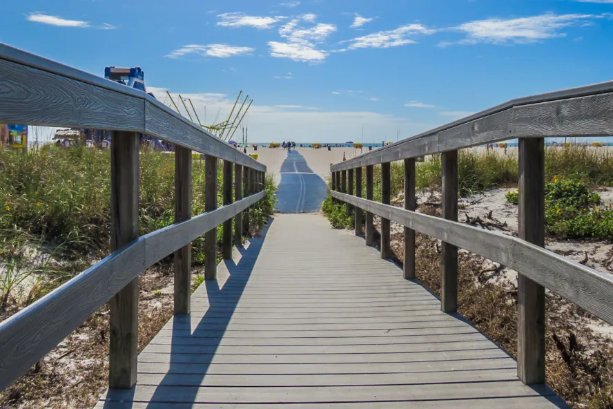 boardwalk to beach lined with dunes, with a large inflatable water slide on the left, the sky is blue with puffy white clouds