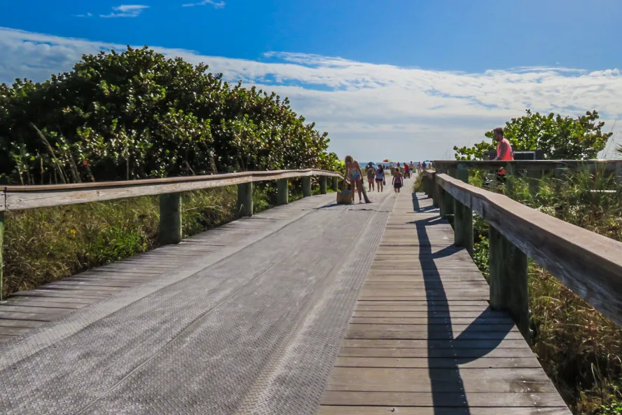 a wooden walkway with a mat surface runs to the sand, with vegetation on either side at Upham Beach