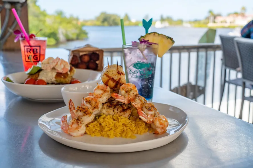 Two seafood dishes and two drinks on a bar overlooking the water at Rusty Bellies.