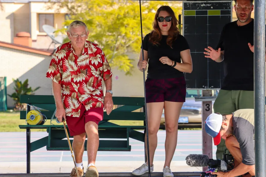 a man in a red hawaiian shirt and shorts plays shuffleboard with several other people