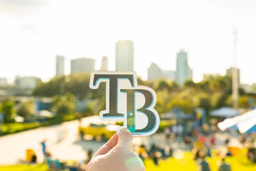 Tampa Bay Rays logo held up against St. Pete skyline