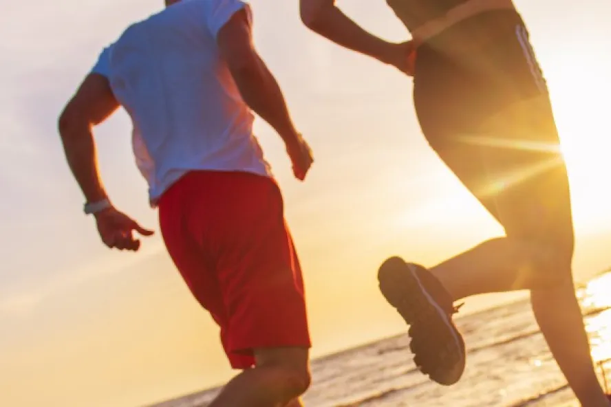 Two people running on the beach with the sunset behind them.