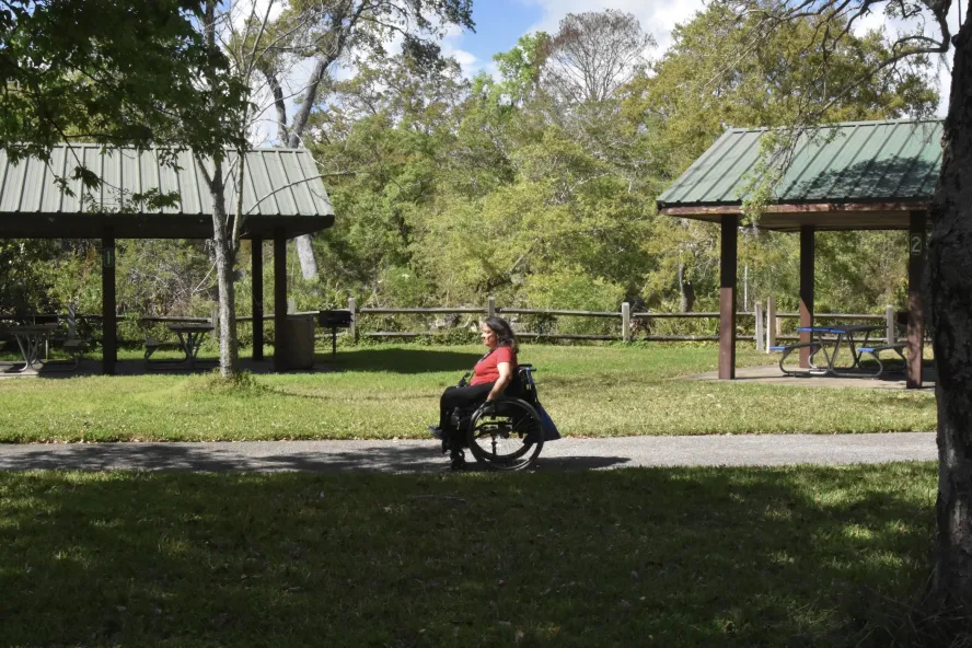 Woman in wheelchair rolls along paved path through park