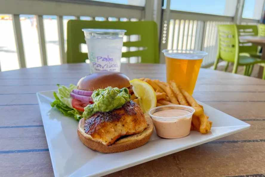 a blackened grouper sandwich with guacamole on top on a brioche bun with fries and a beer at Crabby's Beachside Pavilion in Clearwater Beach