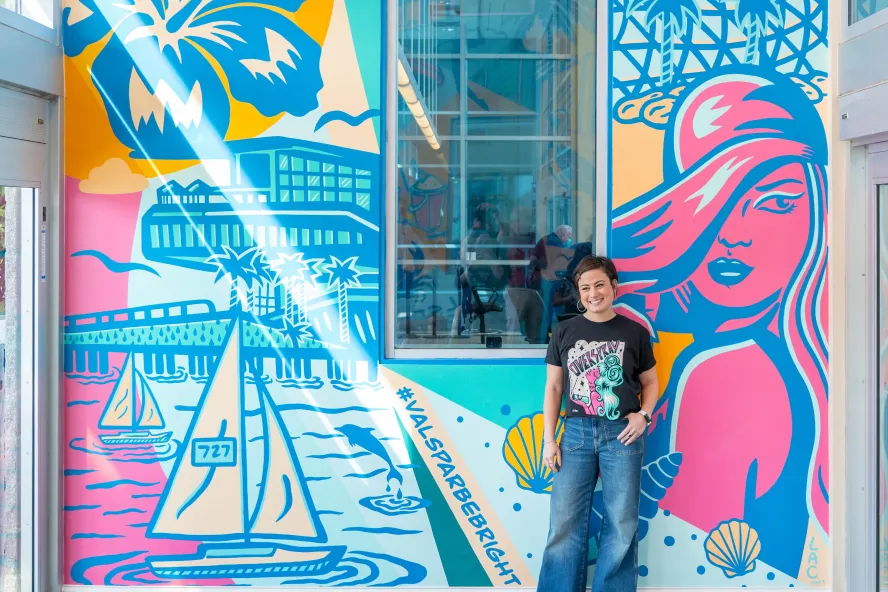 a person in jeans and a black t-shirt stands in front of a pastel colored mural named "be bright" at St. Petersburg Clearwater International Airport