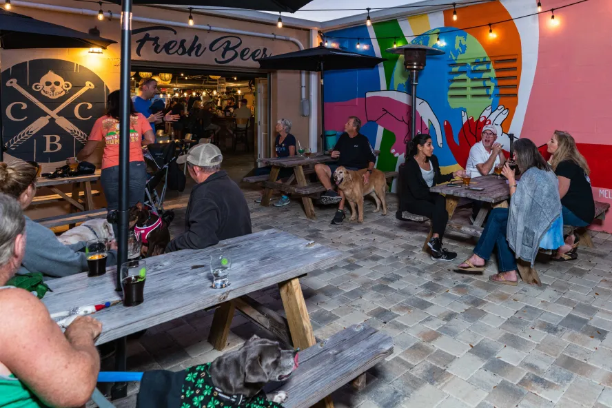 People and dogs sit at picnic tables at brewery's outdoor patio.