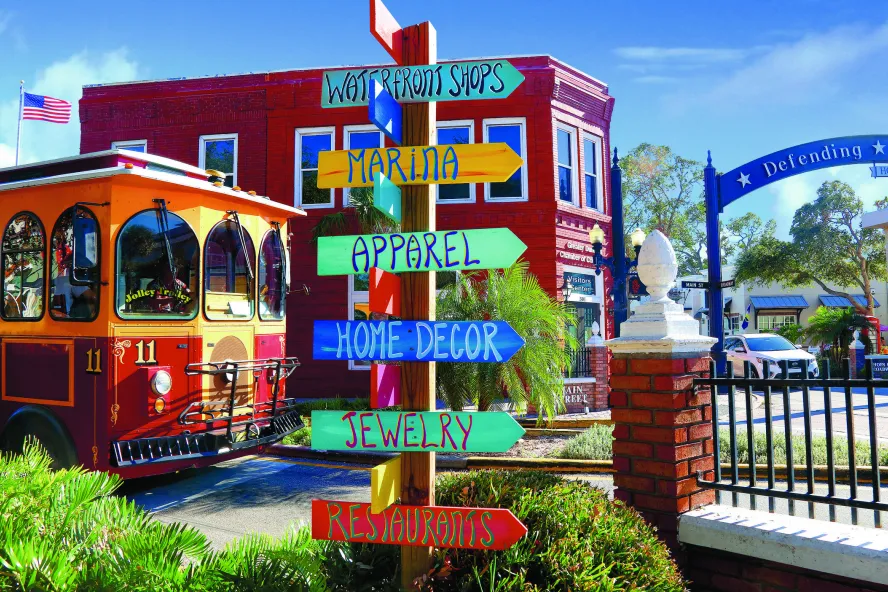 A colorful direction sign is in front of a trolley and shops.