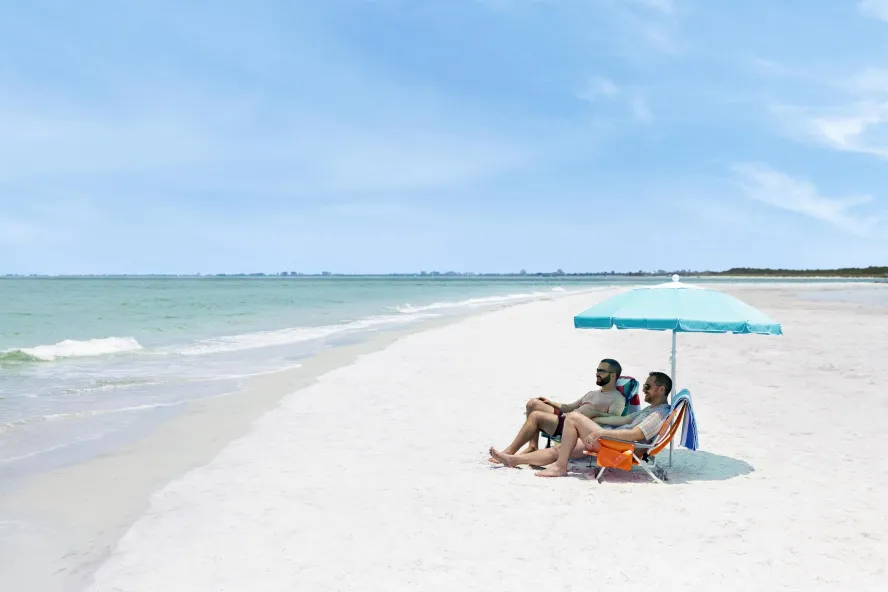 Couple sits under an umbrella on a wide, white-sand beach
