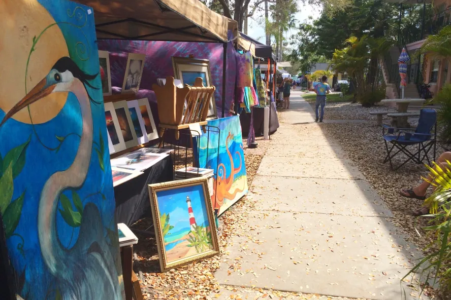 Tents filled with paintings and other artwork for sale line a sidewalk.