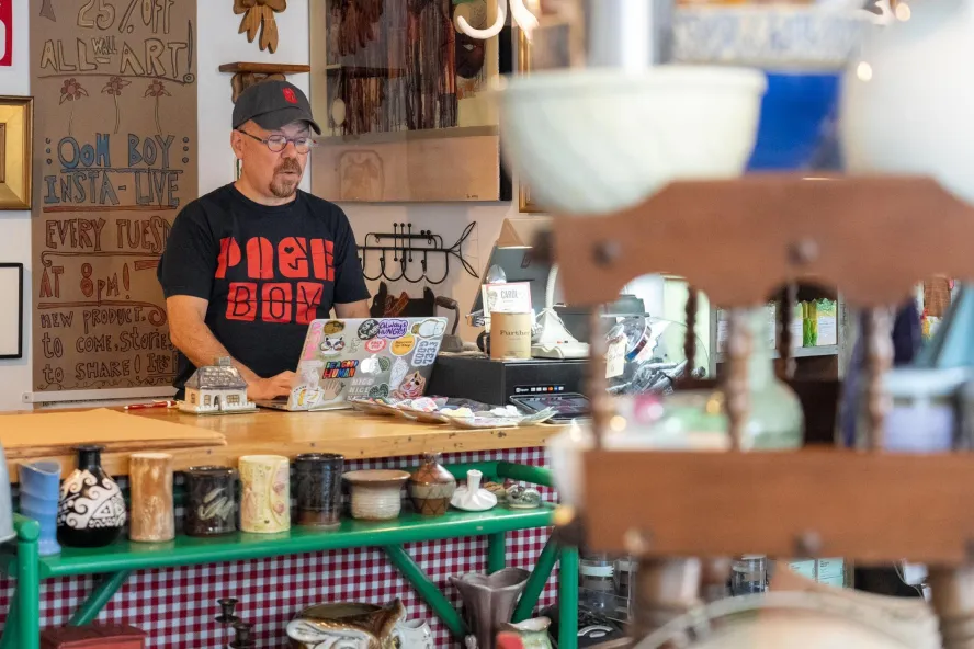 Man behind store counter surrounded by eclectic crafts.