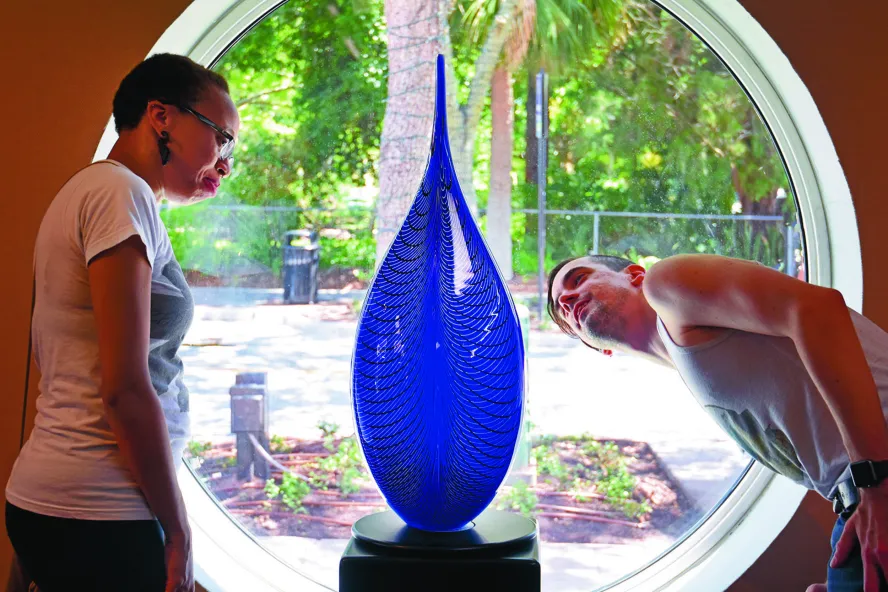 A woman and man look at a tall blue glass sculpture.