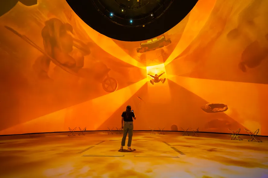 projection in a dome, bright orange, with a woman in front of it 