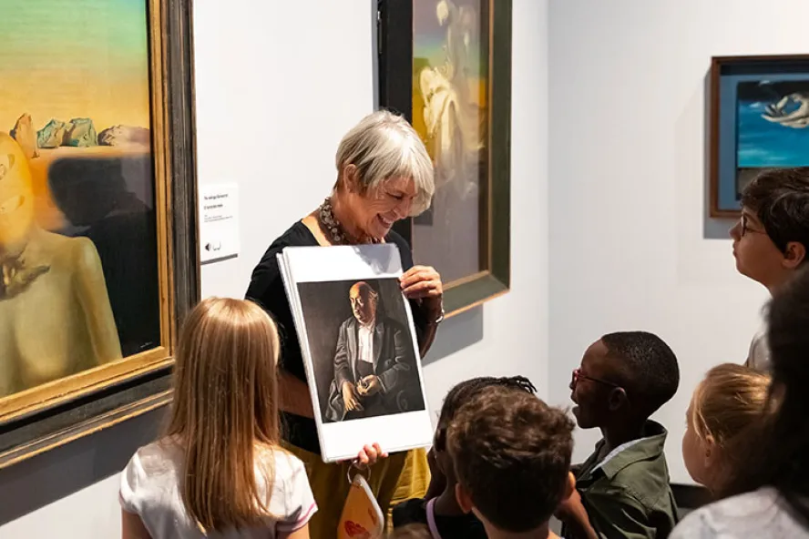 Older woman with short hair showing a group of young kids of painting photo inside a museum.