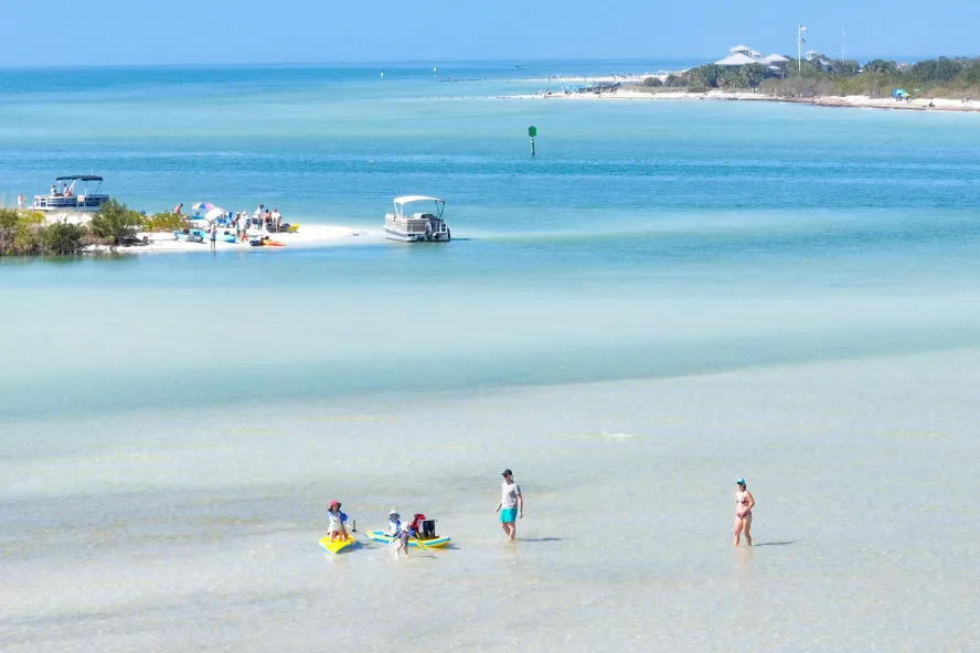 People wade in clear water with two islands nearby.