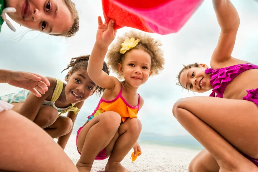 four girls in colorful bathing suits play together at the beach