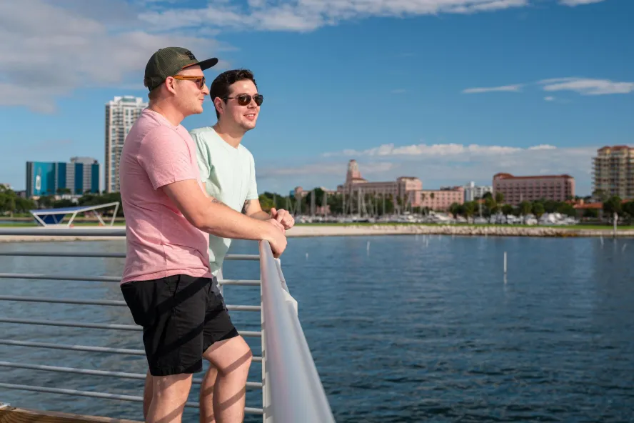 two men stand near a railing looking out over the water near the St. Pete Pier