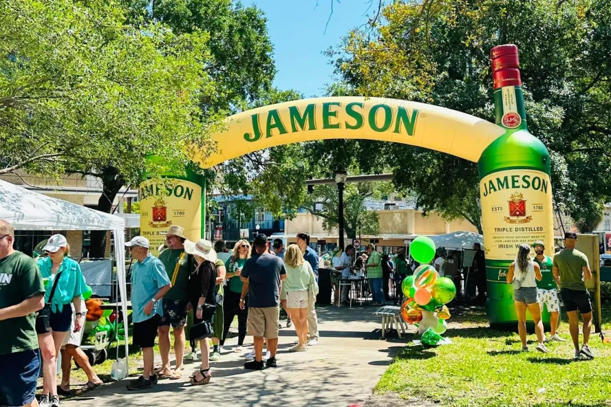 Paddy Fest St. Pete featuring green decorations, a crowd of people and Jameson whiskey blow-up bottle.