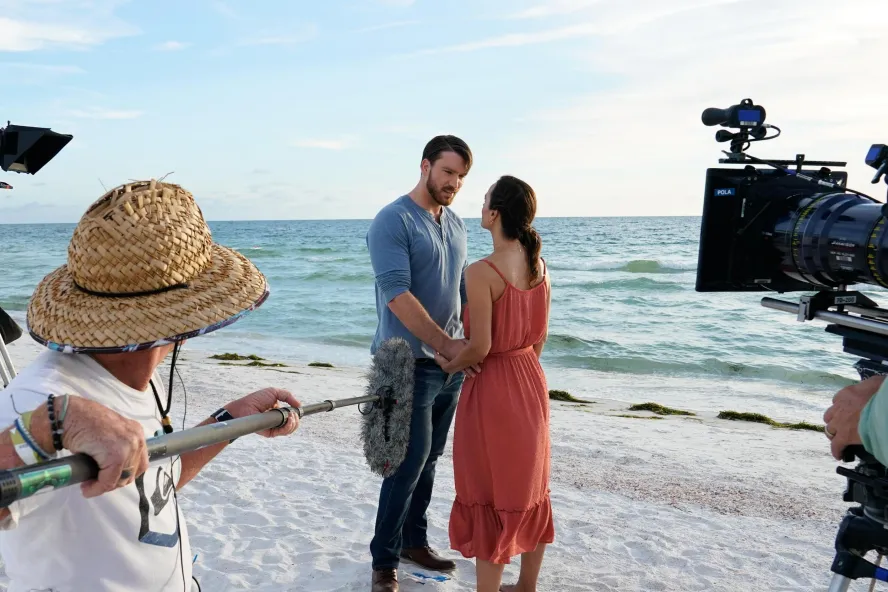 two actors hold hands on the beach while a crew films them for A Taste of Love, a Hallmark movie