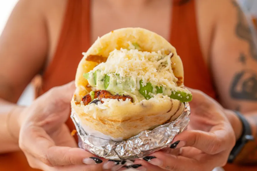 a woman in a tank top holds a large arepa in her hands