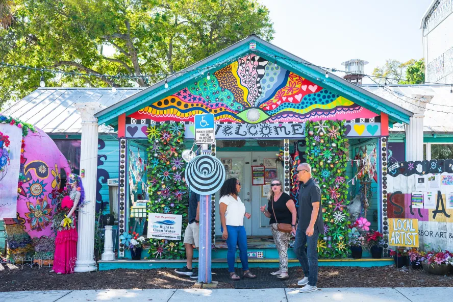 three people stand outside a brilliantly colored and whimsical building