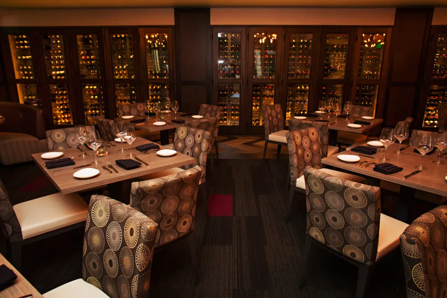 A dim moody dining room with a wine wall in the backdrop