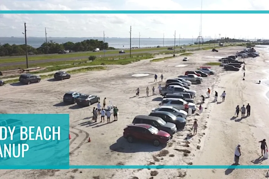 Aerial shot of multiple cars parked on a beach with volunteers cleaning up.