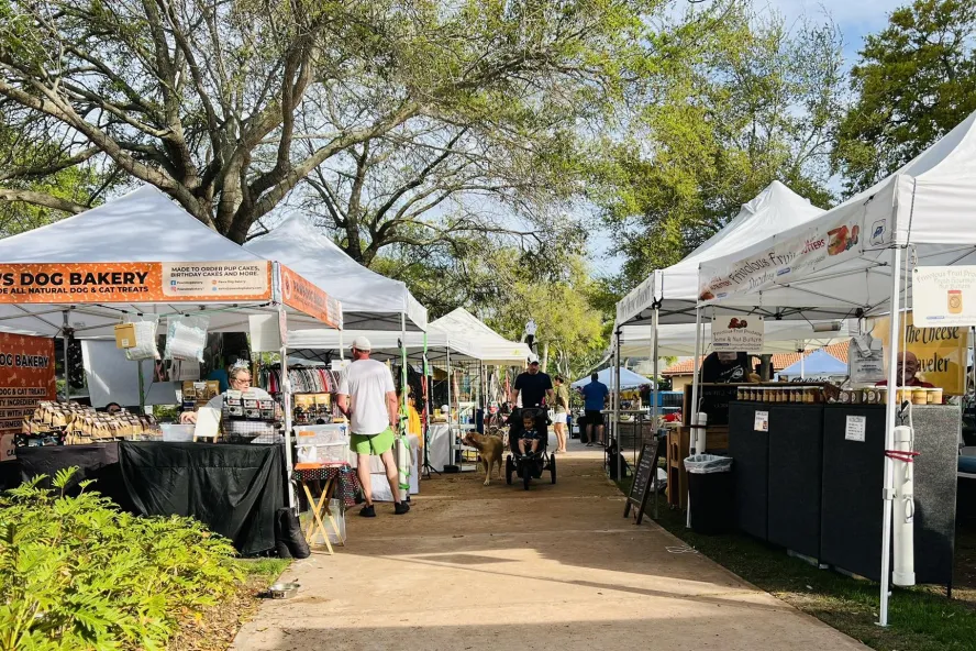 People walking at an outside market featuring many white vendor tents.