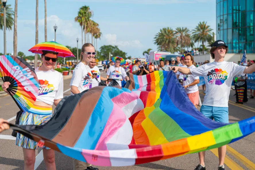 people in rainbow colored clothing carrying a pride flag in a parade