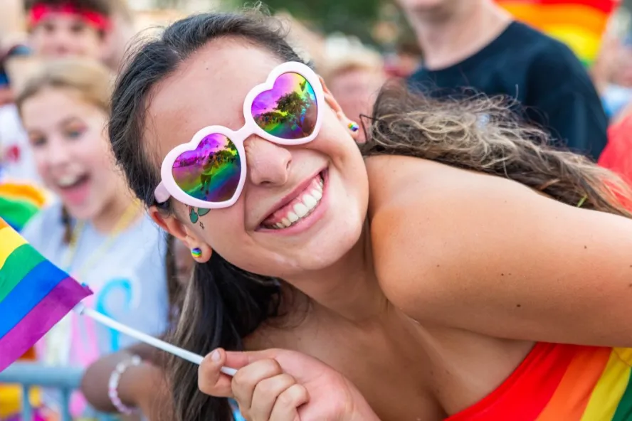 LGBTQ+ parade visitor holding a rainbow flag and smiling at the camera.