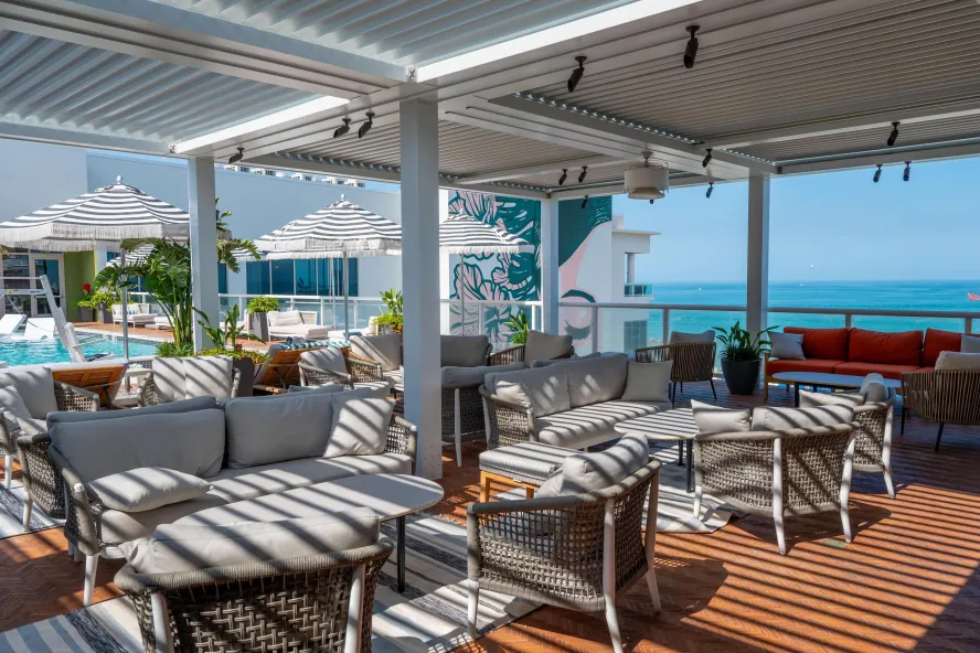 a beautiful rooftop bar with tables and chairs next to a swimming pool with umbrellas for shade with a view of the turquoise gulf of mexico