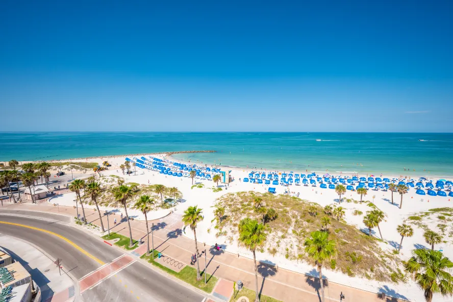 Rows of blue umbrellas dot the white sand beach under a clear sky at The Hiatus Clearwater Beach