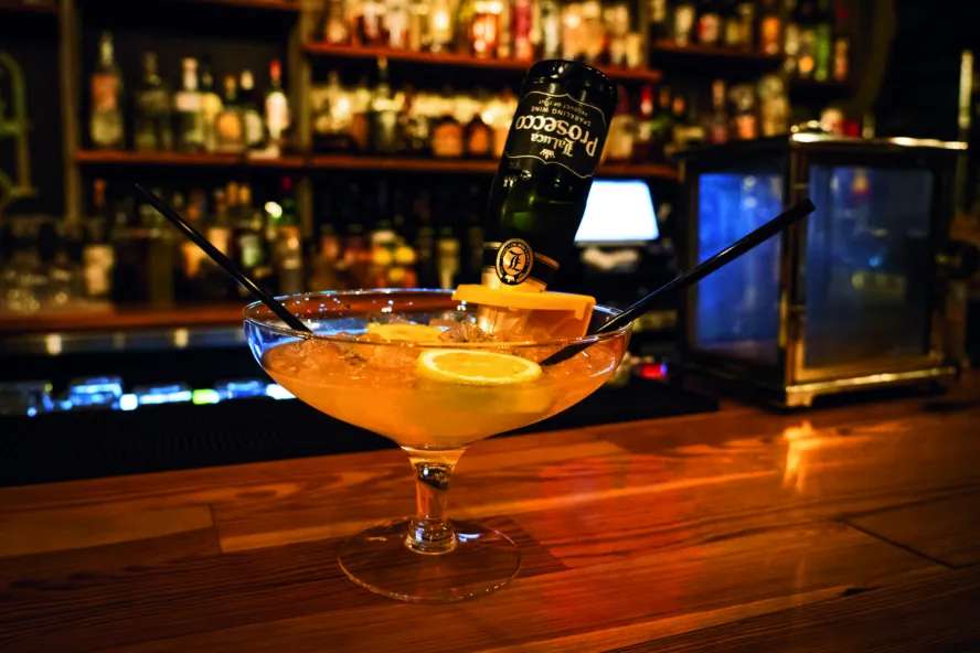 A photo of a pink cocktail with two straws on a bar