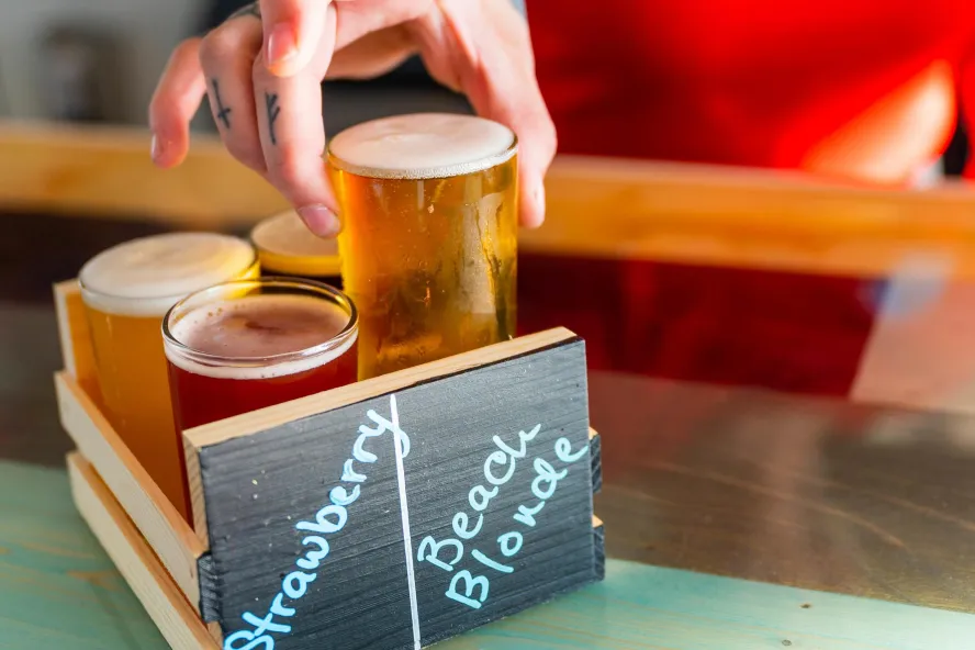 a flight of 4 different flavored beers in a carrying box with a person's hand placing a beer inside