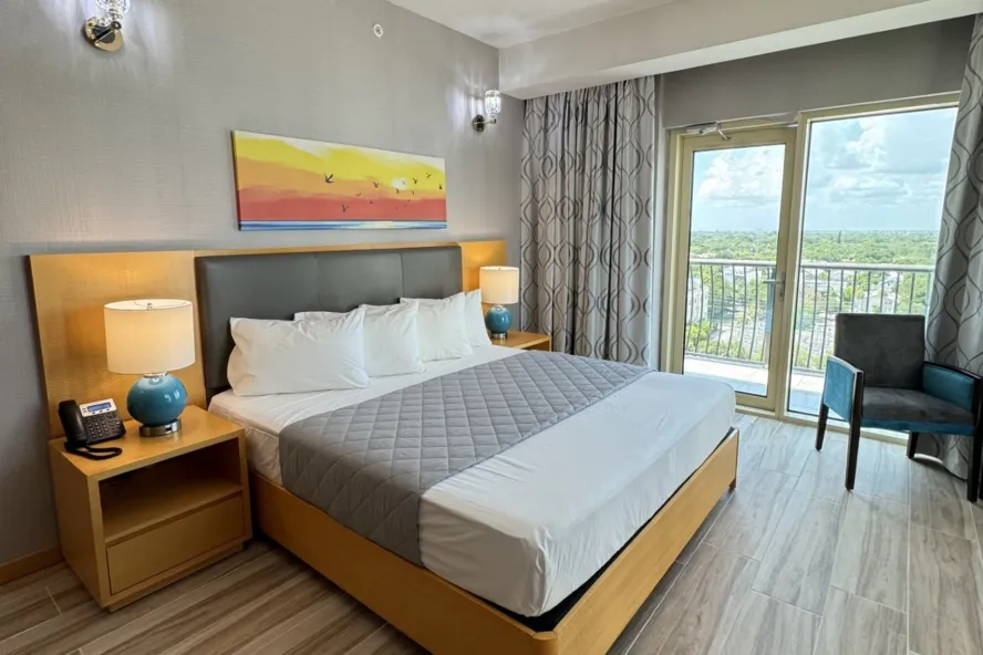 image of hotel room with clean modern furniture and white bedding with a glass sliding door with a view of downtown St. Pete