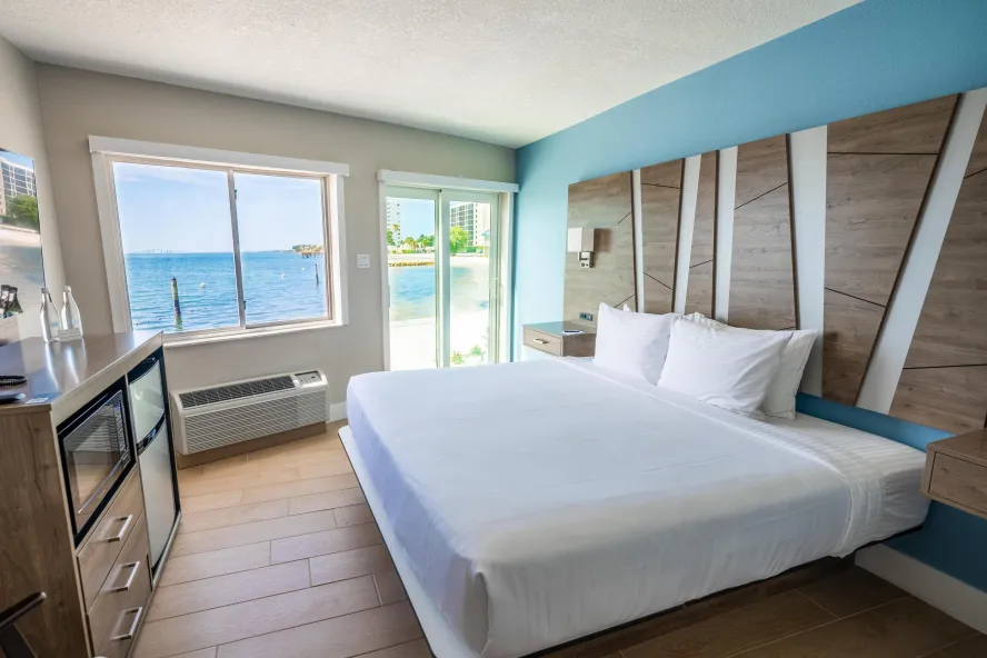 a hotel room with a bed with white linens and a modern geometric headboard with a great view of the blue bayfront waters
