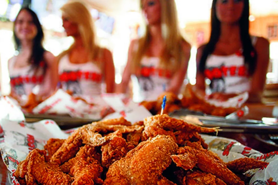 A plate of chicken wings and Hooters waitresses in the background