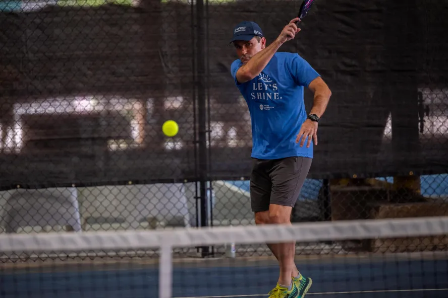 a man in a blue shirt and hat playing pickleball