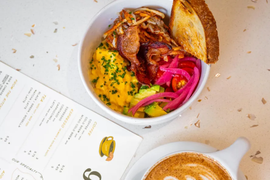 an artfully prepared breakfast bowl next to a menu and a pretty cup of latte