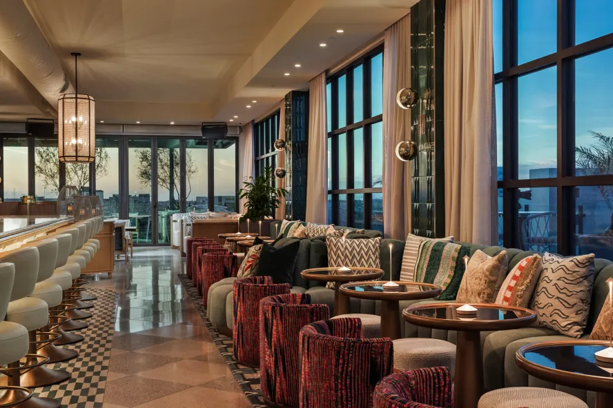 a stylish bar with small tables to the side and views of a city through large windows