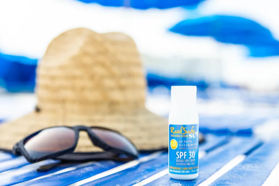 a beach towel with a straw hat, dark sunglasses and a small bottle of reef-safe sunscreen
