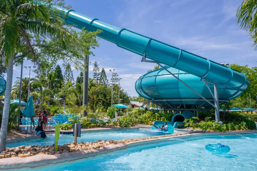 blue water slide declining down into a large bowl into blue waters of pool below surrounding by green palm trees at Aquatic water park in Orlando.