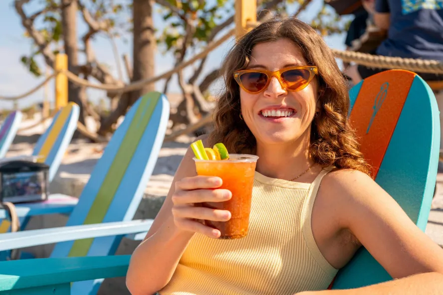 A woman in a beach chair holds up a cocktail.