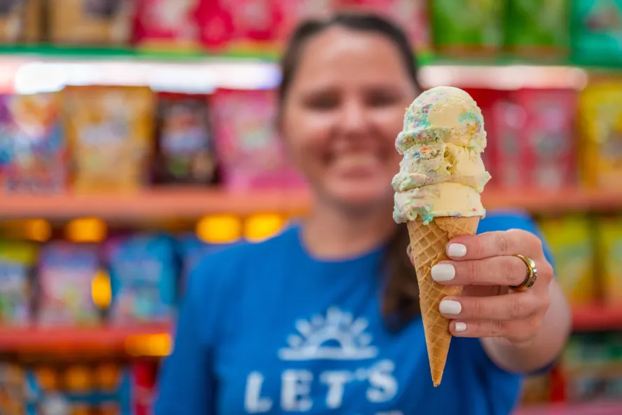 a person in a blue Tshirt holding out a stacked ice cream cone at Candy Kitchen