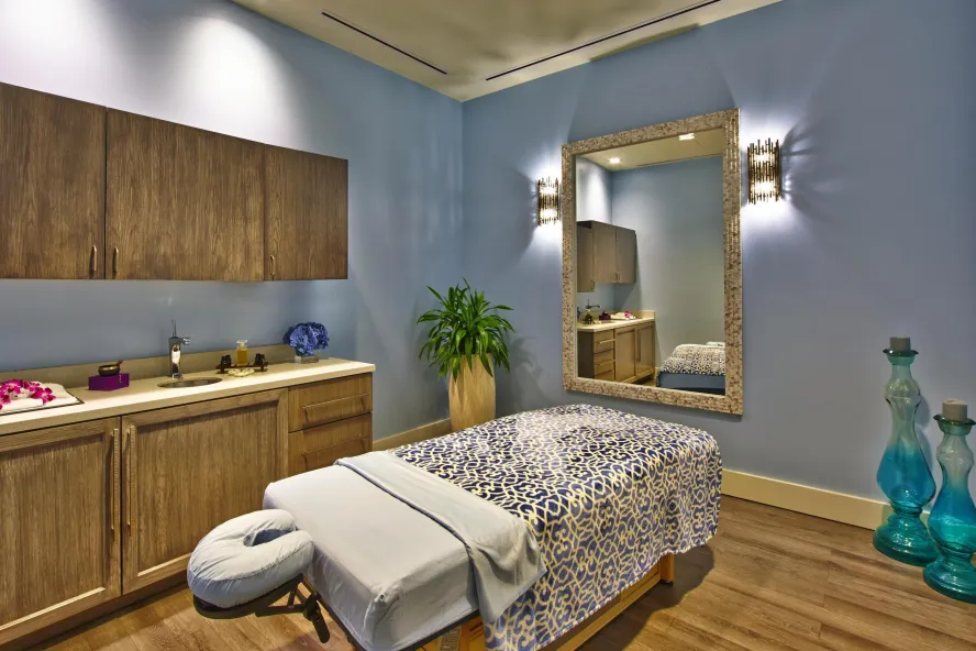 an elegant spa treatment room in soothing wood tones with a massage table that has a black and white blanket on top of it