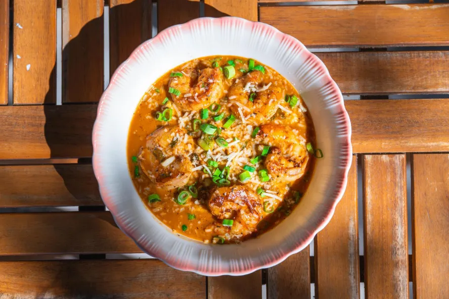 a pink and white bowl with ruffled edges containing a delicious-looking shrimp jambalaya with a rich orange rough and chives on top as a garnish